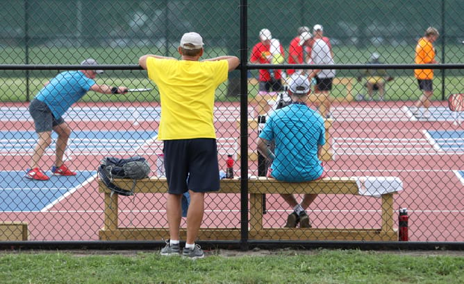 Children spectating pickleball game behind the fence